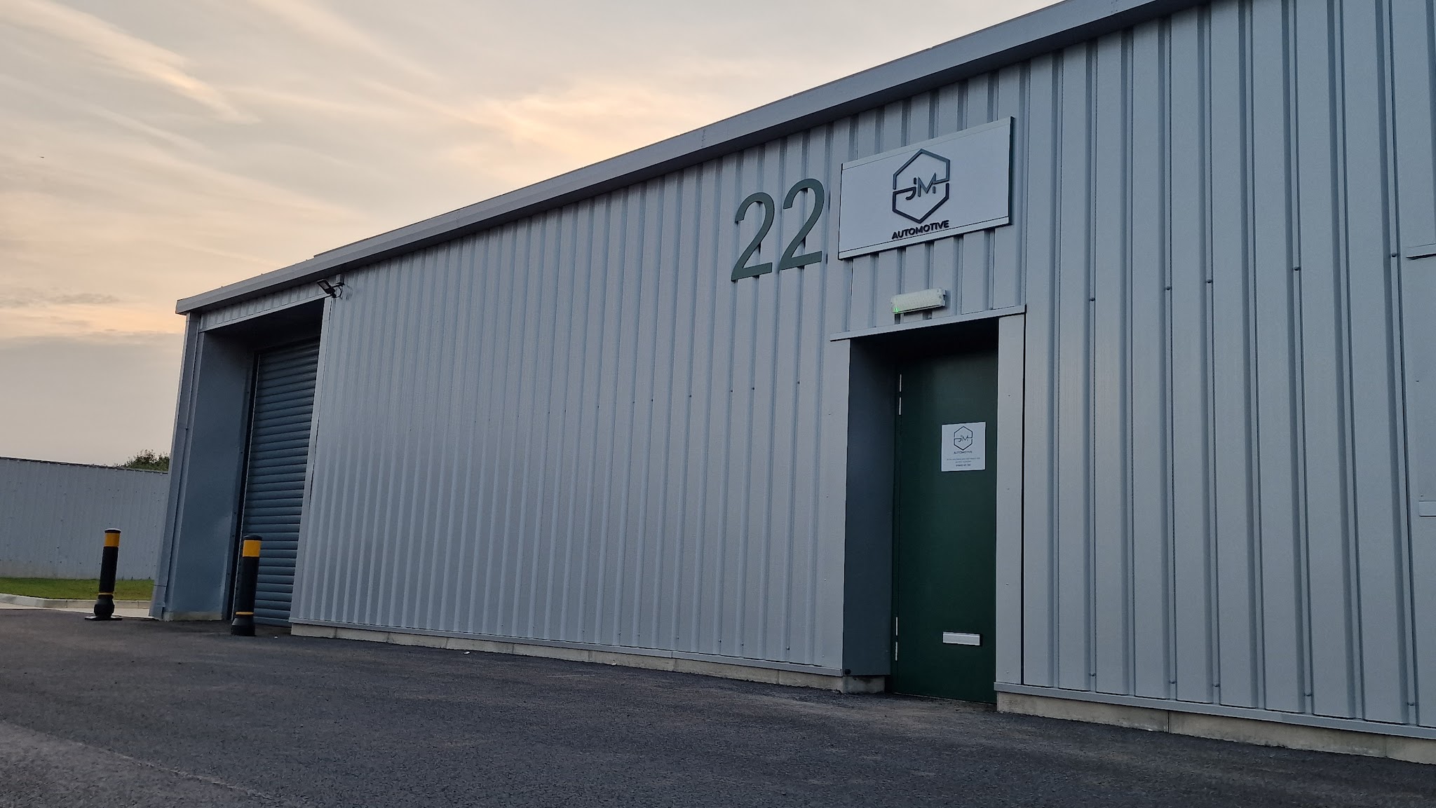 JMM Automotive's grey unit at number 22 at dusk, with the JM sign above the green door and the roller shutter