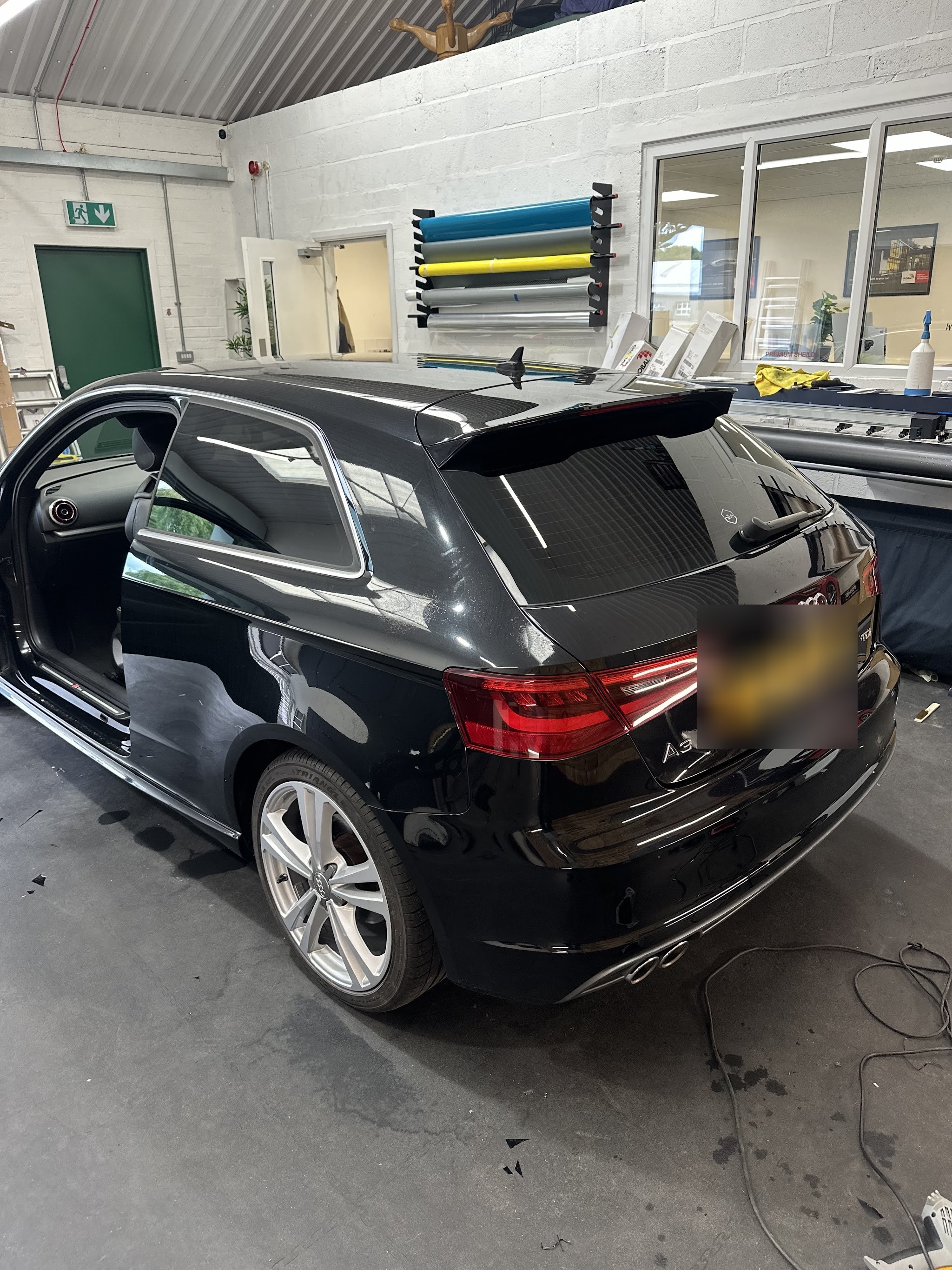 A black Audi A3 Sportback with its door open inside a clean workshop bay