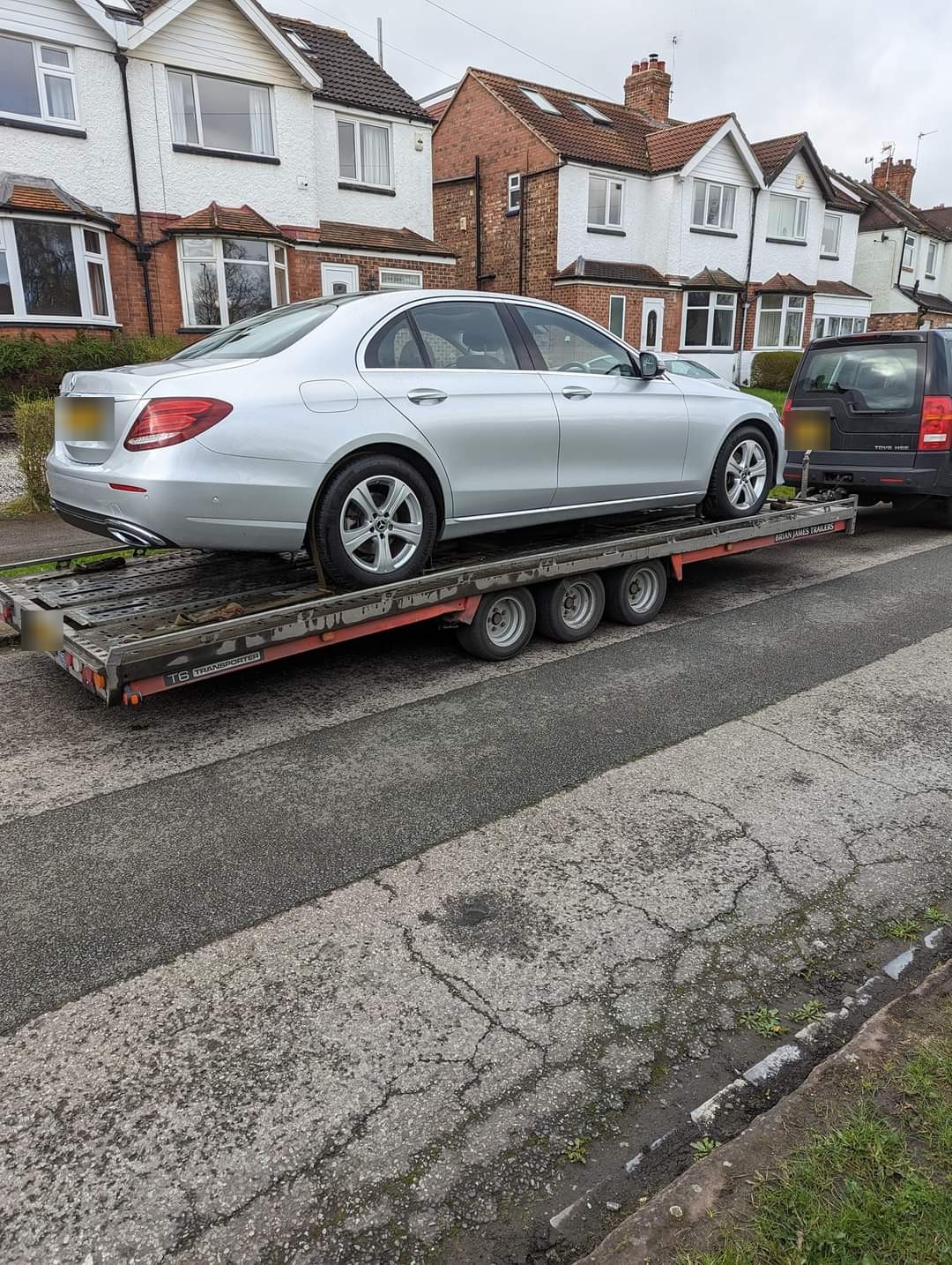 A silver Mercedes saloon strapped onto a flatbed car trailer, delivered to a residential street